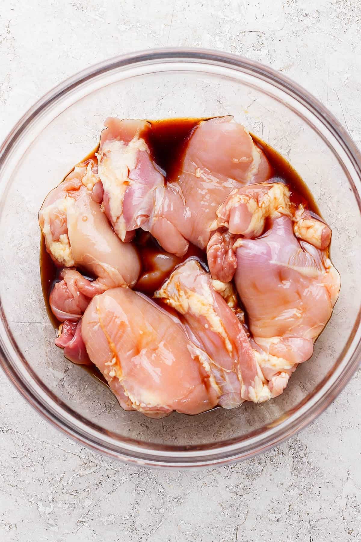 Chicken thighs marinating in soy sauce in a bowl for bang bang chicken salad.