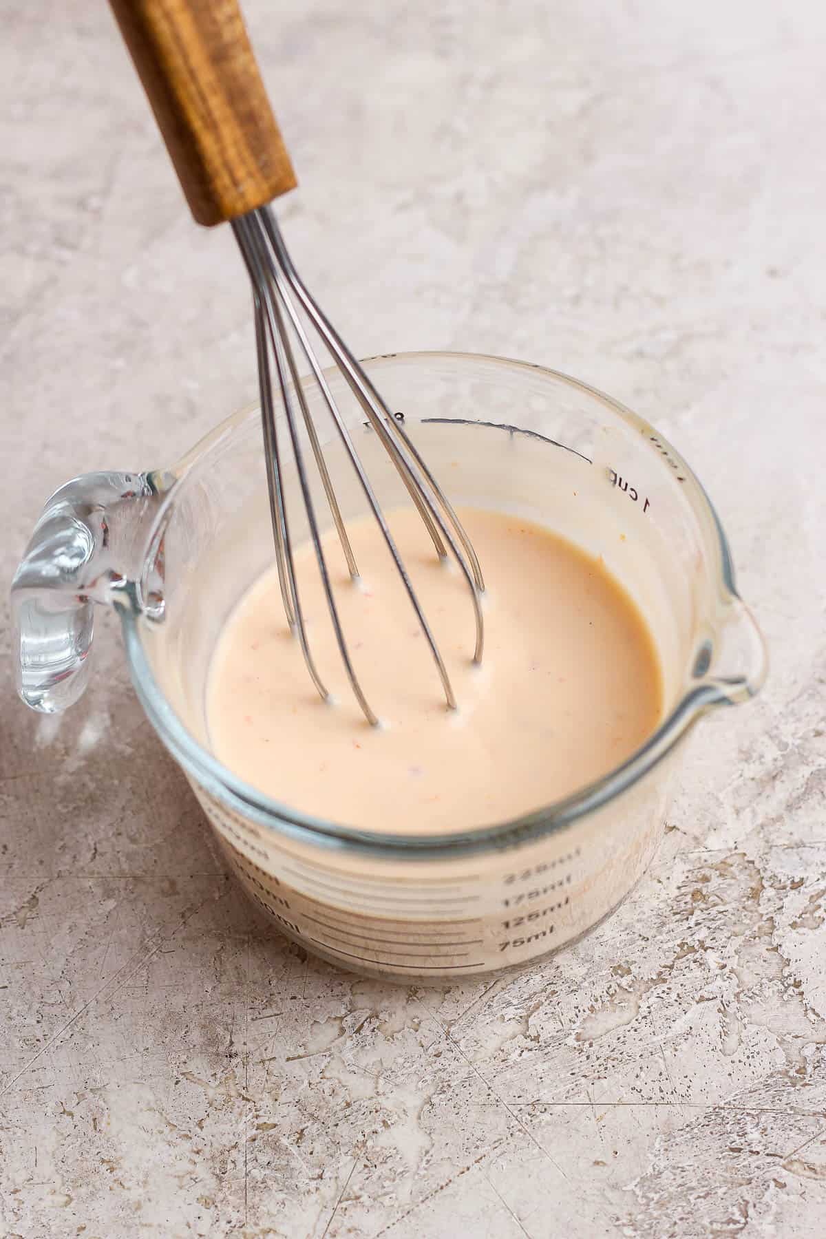 A whisk in a measuring cup of bang bang dressing for bang bang chicken salad.