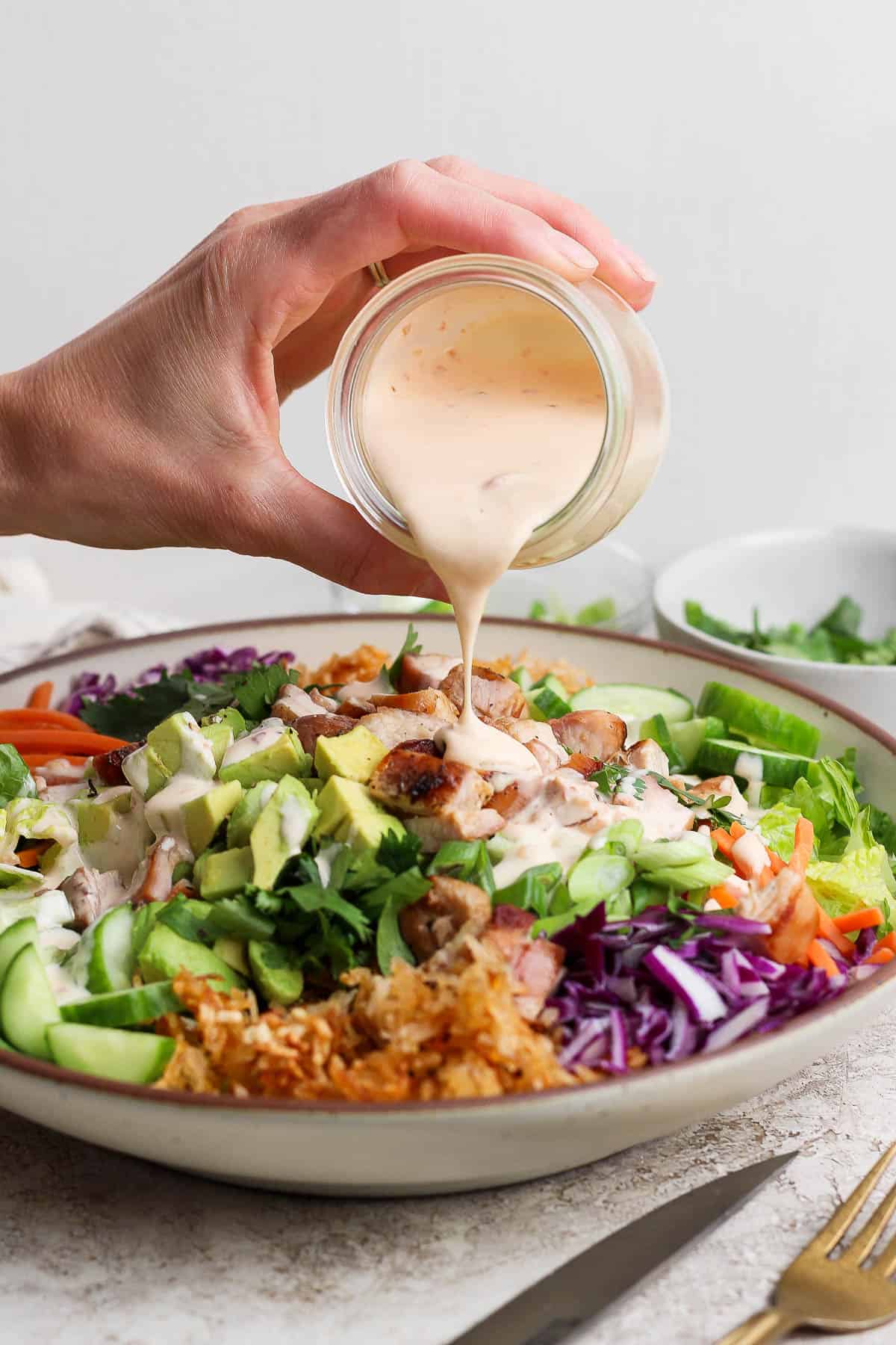 Someone pouring dressing over bang bang chicken salad with crispy rice.