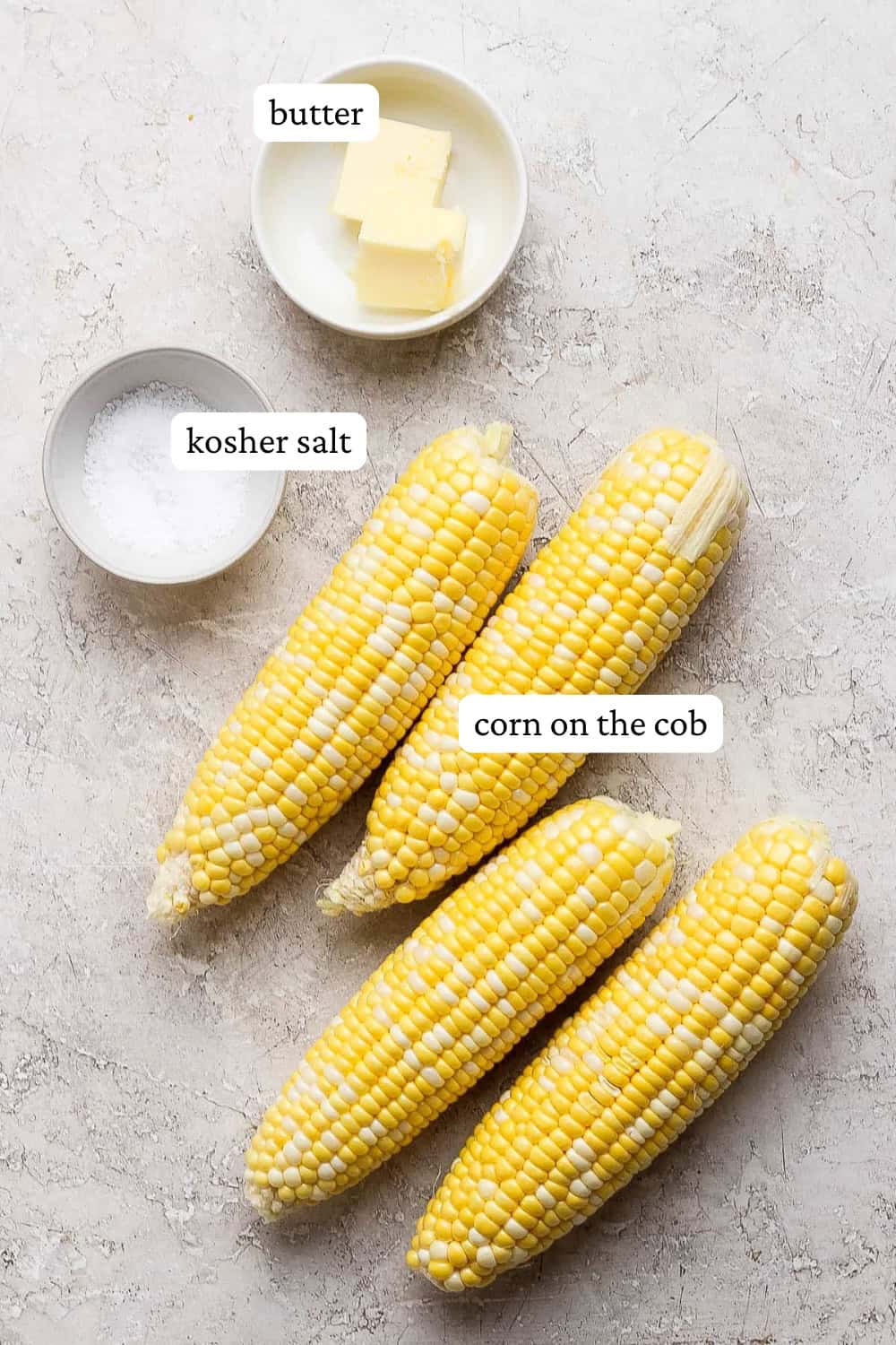 Shucked ears of corn on the counter next to small bowls of salt and butter with labels to make Blackstone corn on the cob.