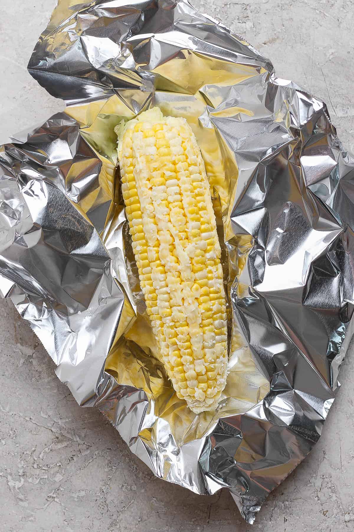 An ear of Blackstone corn on the cob rubbed with butter on a piece of foil before being cooked.
