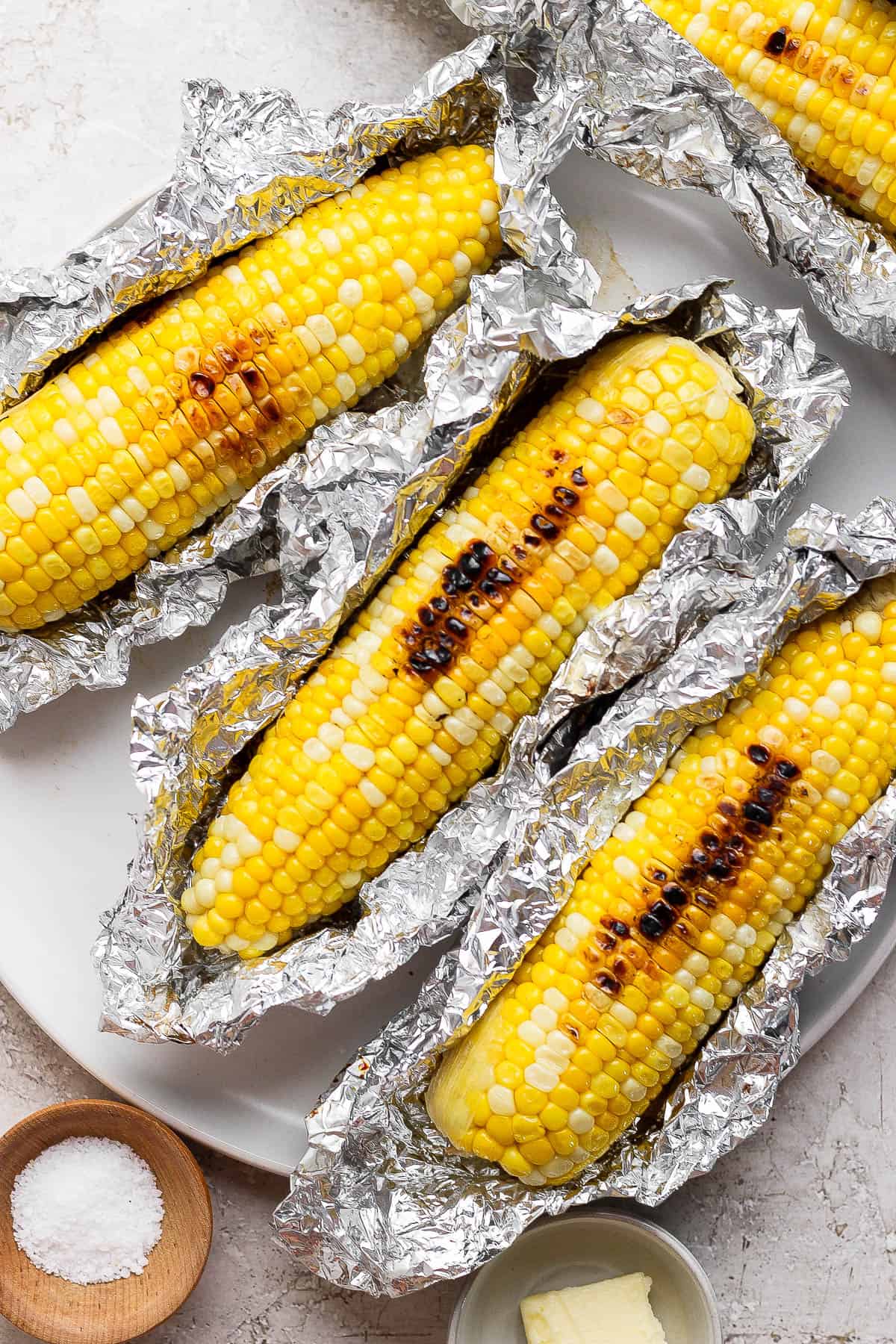 Blackstone corn on the cob sitting on a plate with the foil opened to show the corn.