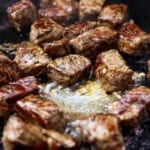 Blackstone steak bites cooking with some melted butter on the griddle.