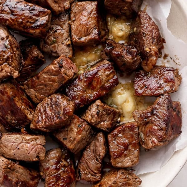 Several Blackstone steak bites in a bowl lined with parchment paper and melted cowboy butter.