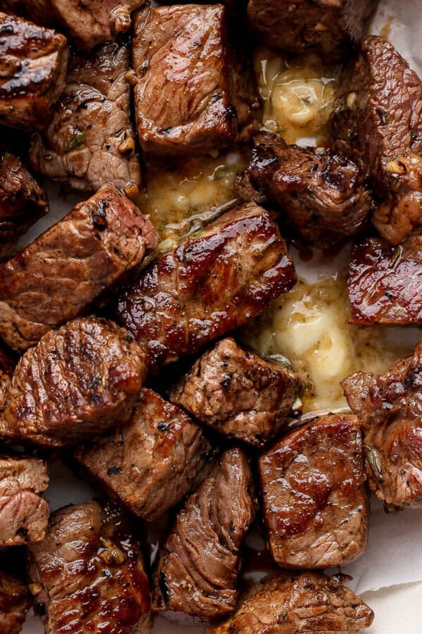 Several Blackstone steak bites in a bowl lined with parchment paper and melted cowboy butter.