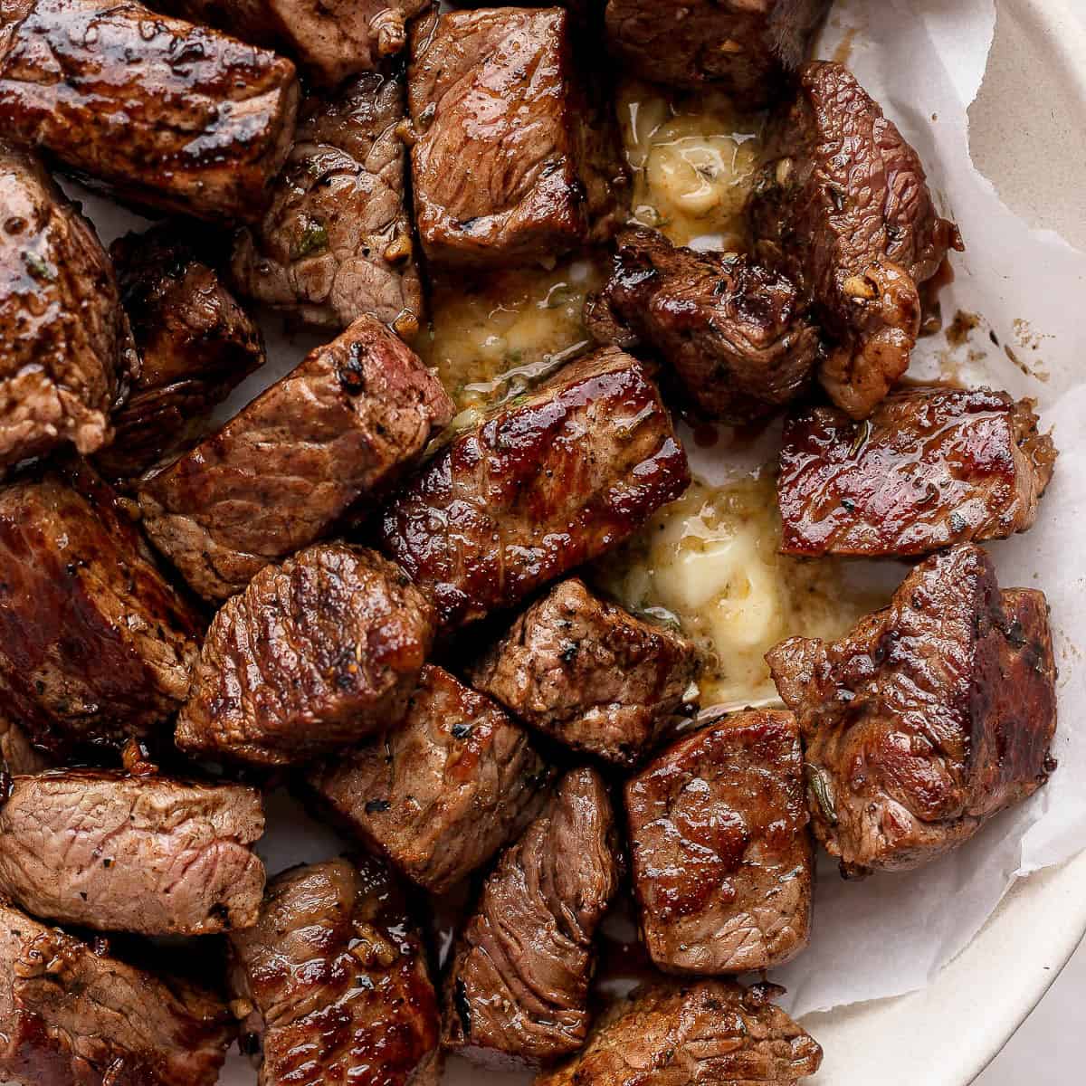 Several Blackstone steak bites in a bowl lined with parchment paper and melted cowboy butter.