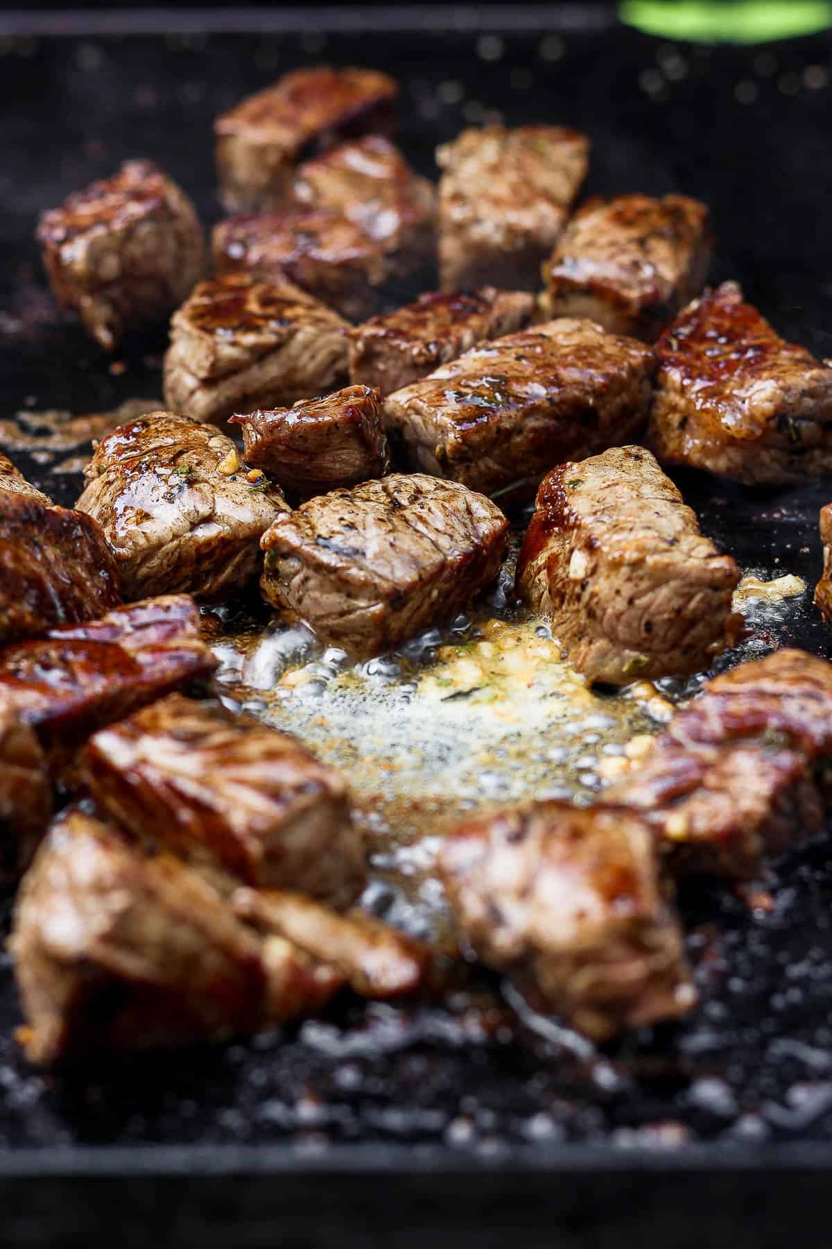 Blackstone steak bites cooking on a hot cooktop with some cowboy butter.