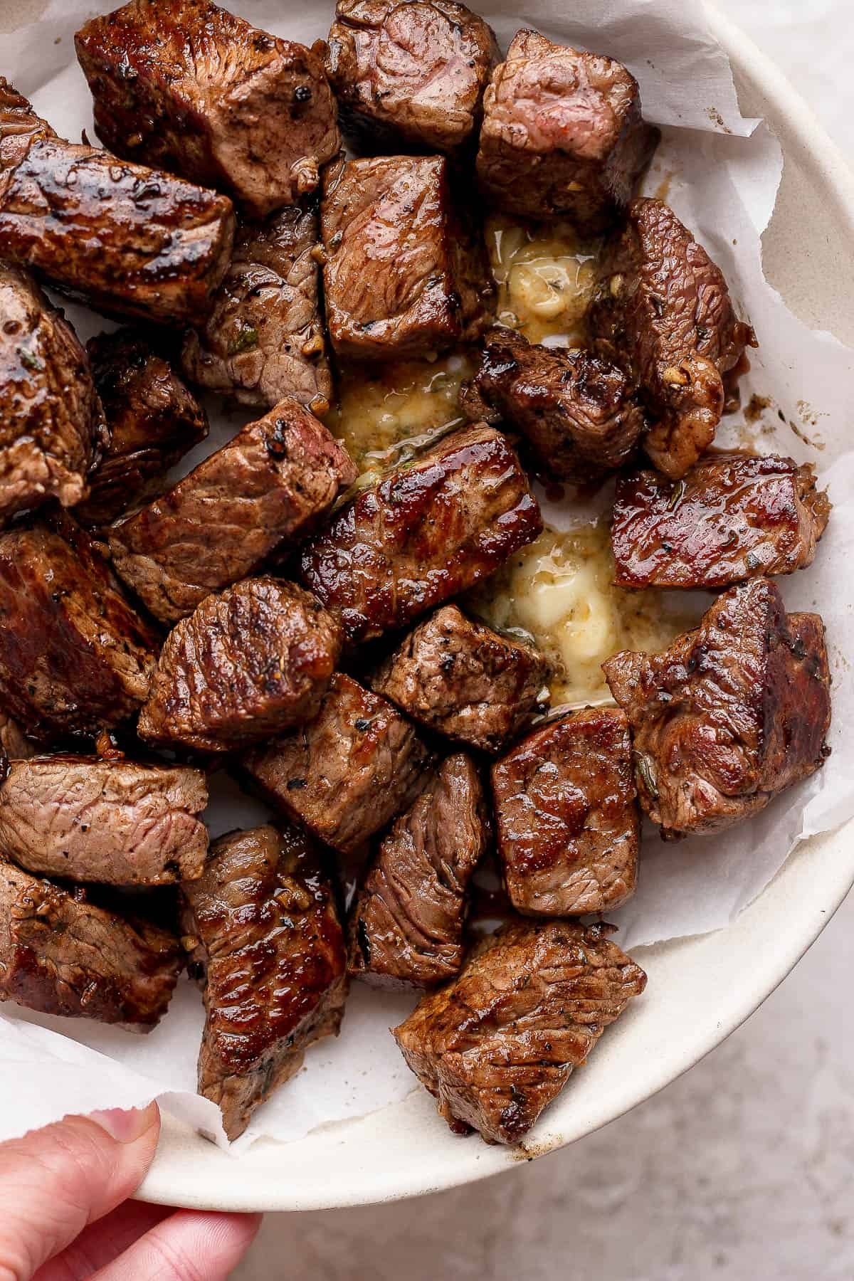 Blackstone steak bites resting with melted cowboy butter in a parchment-lined bowl.
