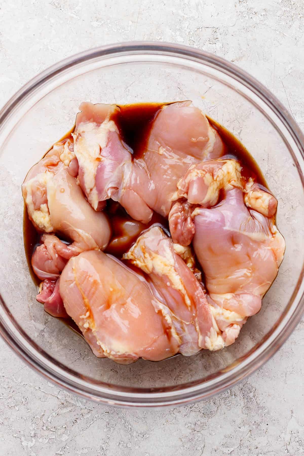 Chicken thighs marinating in a large glass bowl before being cooked to make Blackstone teriyaki chicken.