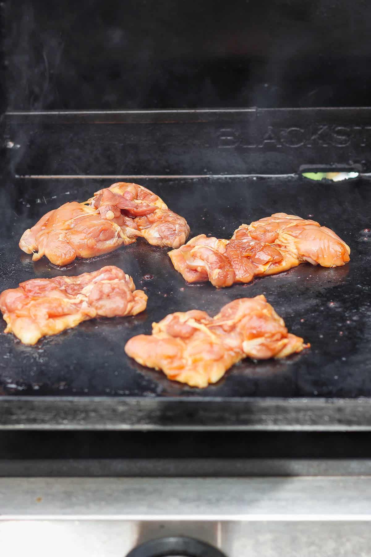 Marinated chicken thighs searing on a Blackstone to make Blackstone teriyaki chicken.