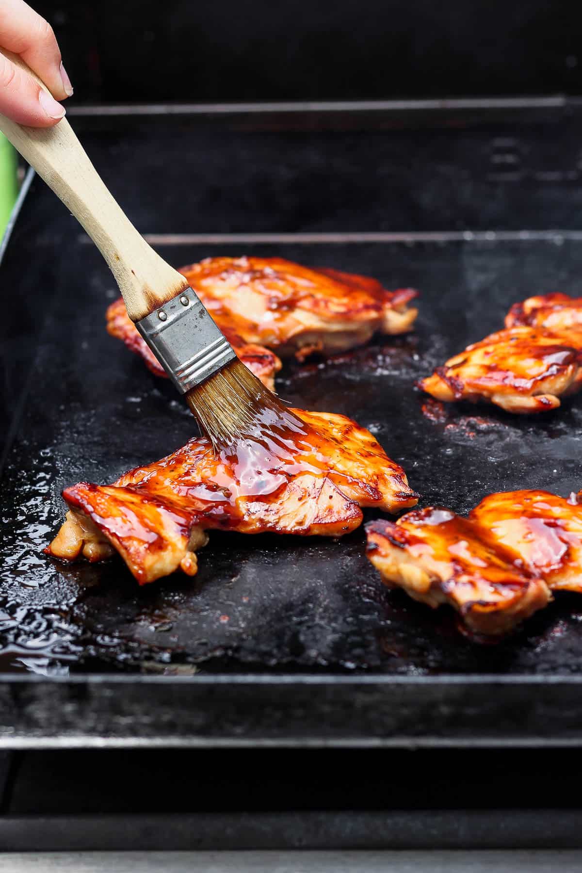 Teriyaki sauce being brushed on Blackstone teriyaki chicken thighs.