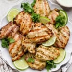 Several cilantro lime chicken thighs on a platter with lime wedges and fresh cilantro.