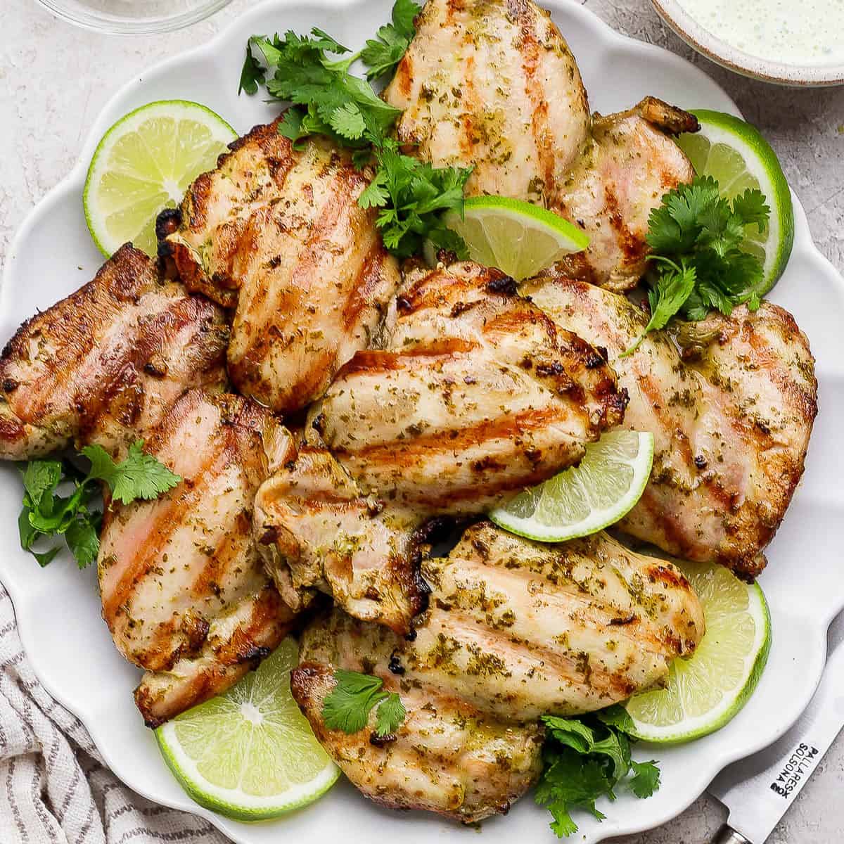 Several cilantro lime chicken thighs on a platter with lime wedges and fresh cilantro.