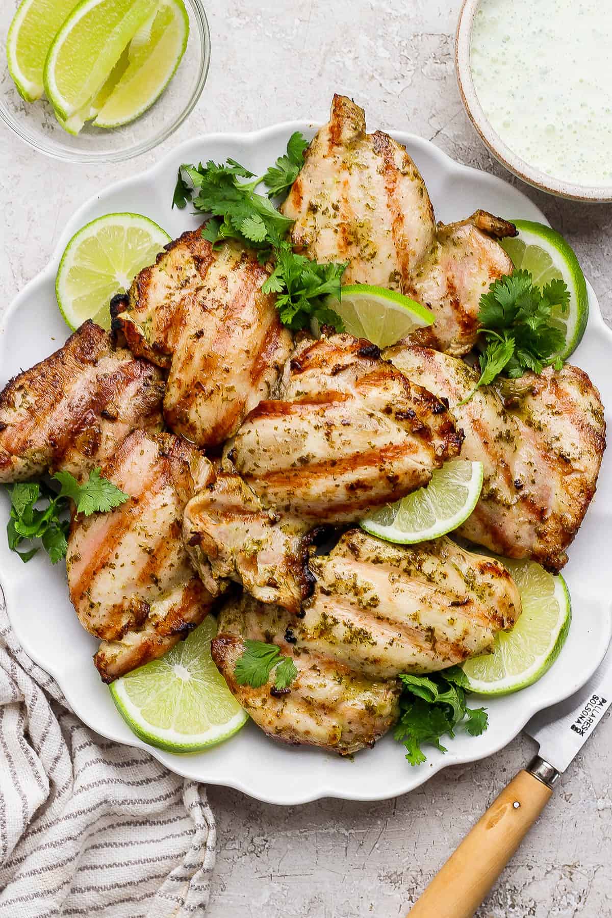 Grilled cilantro lime chicken thighs on a platter with fresh cilantro and slices of lime.