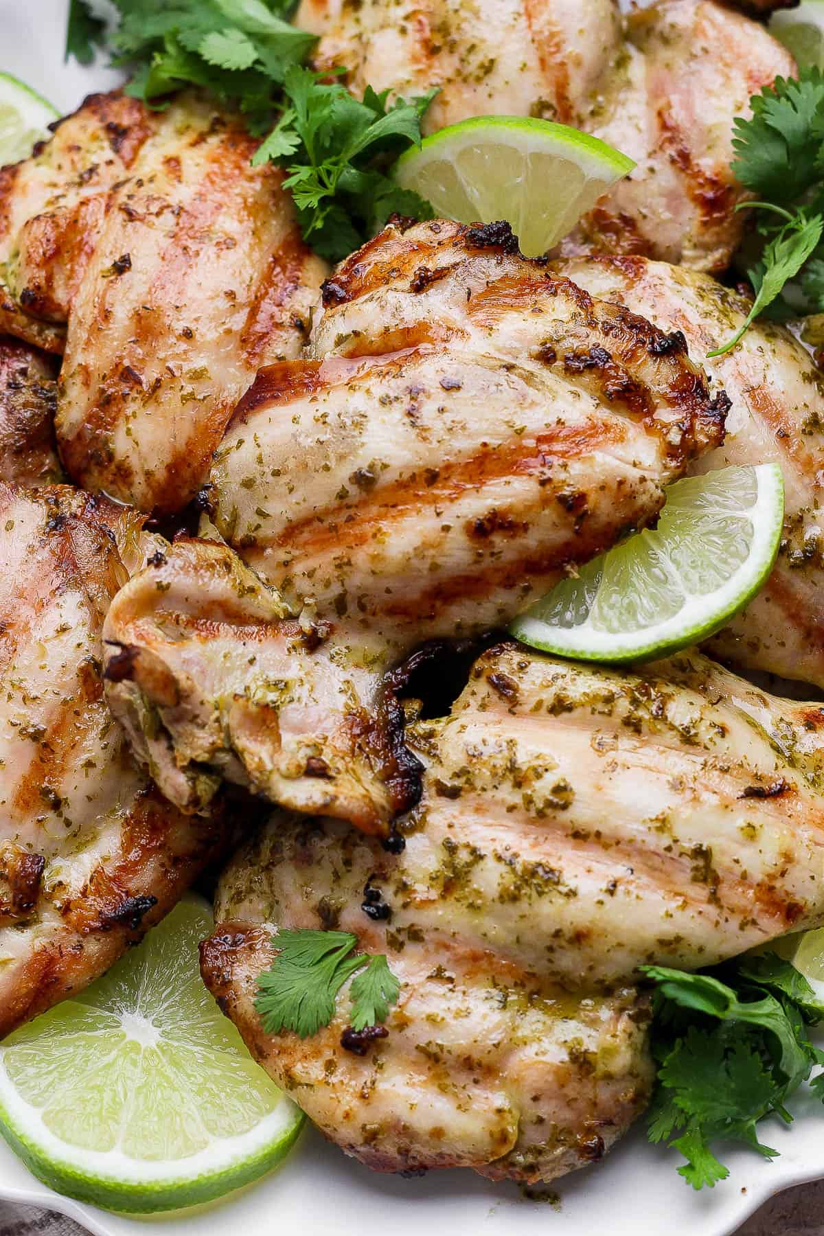 Several grilled cilantro lime chicken thighs on a platter with lime slices and fresh cilantro.