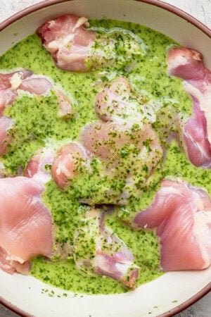 Cilantro lime marinade over several boneless skinless chicken thighs in a large bowl.