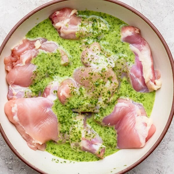 Cilantro lime marinade over several boneless skinless chicken thighs in a large bowl.