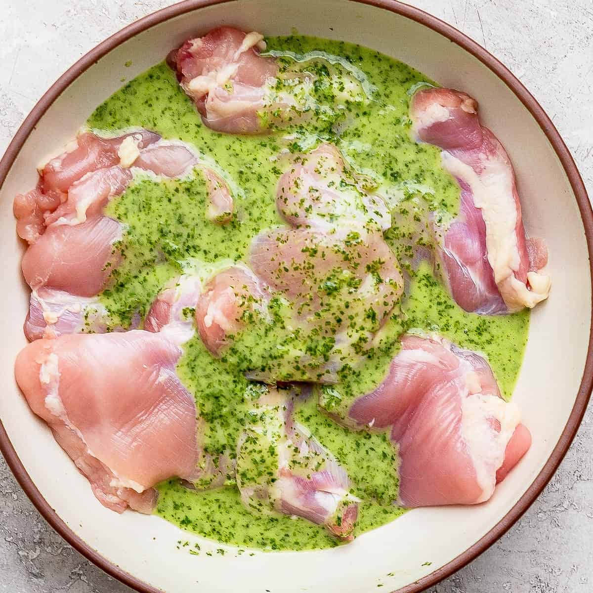 Cilantro lime marinade over several boneless skinless chicken thighs in a large bowl.