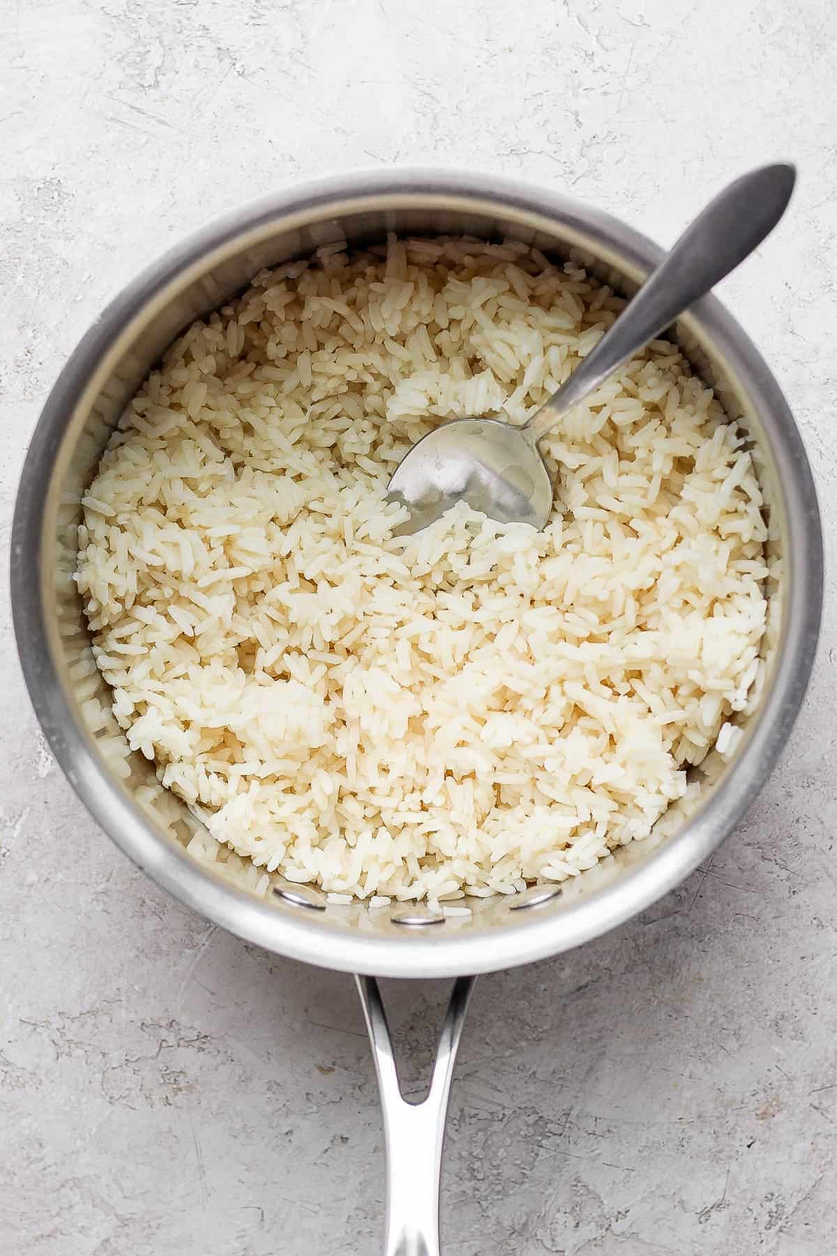 Cooked white rice in a pot with a spoon sticking out the side.