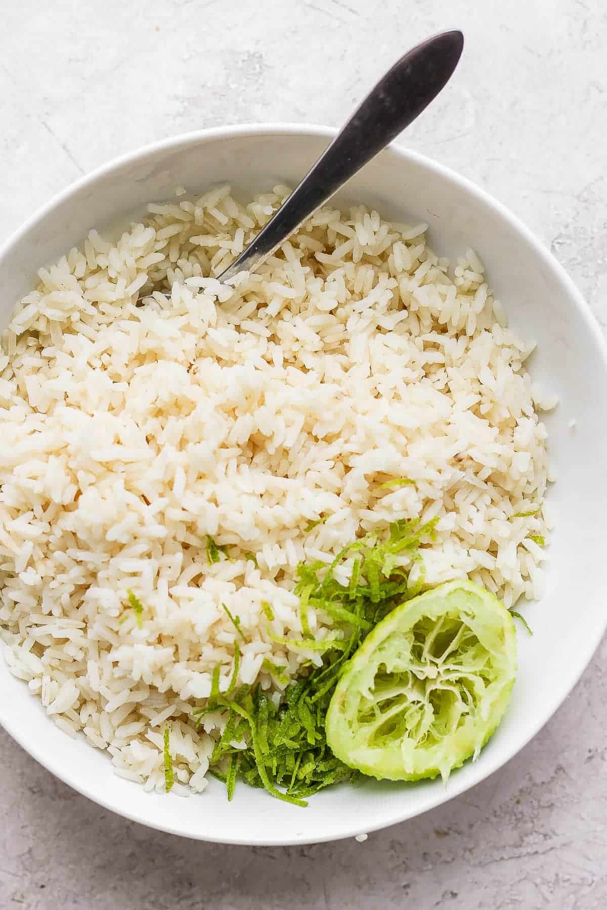 Cooked rice in a bowl with lime zest, half a squeezed lime, and a spoon sticking out the side.