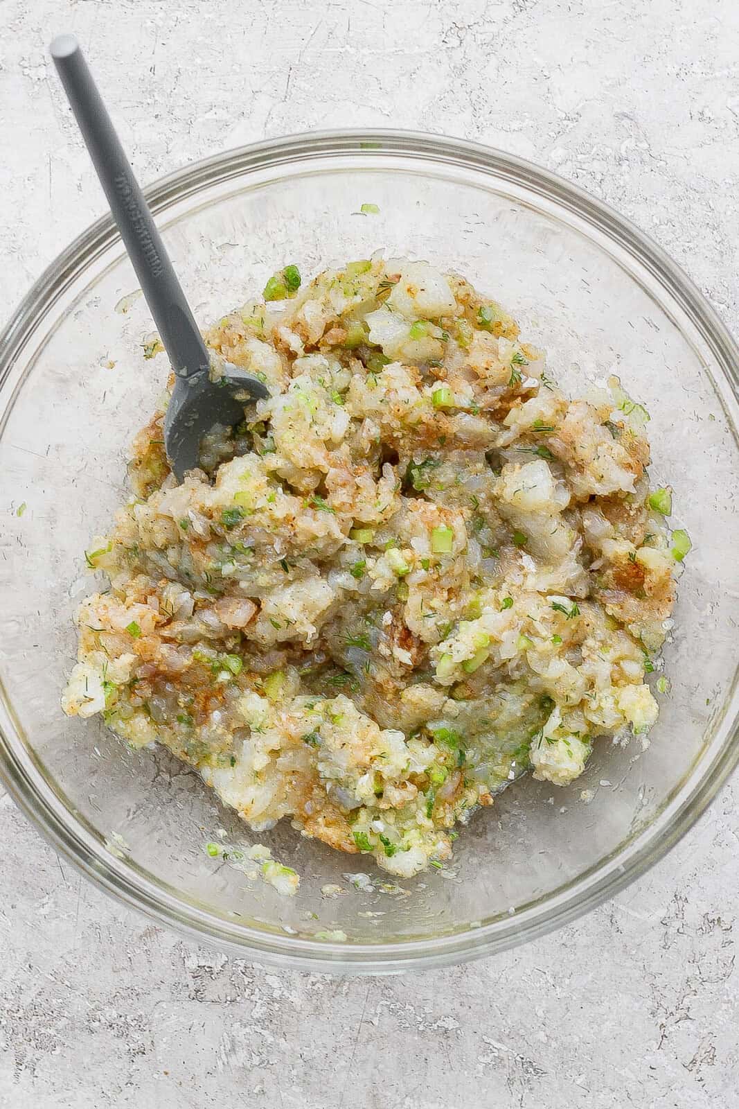 Ingredients for cod cakes in a bowl, mixed and with a spatula sticking out. 