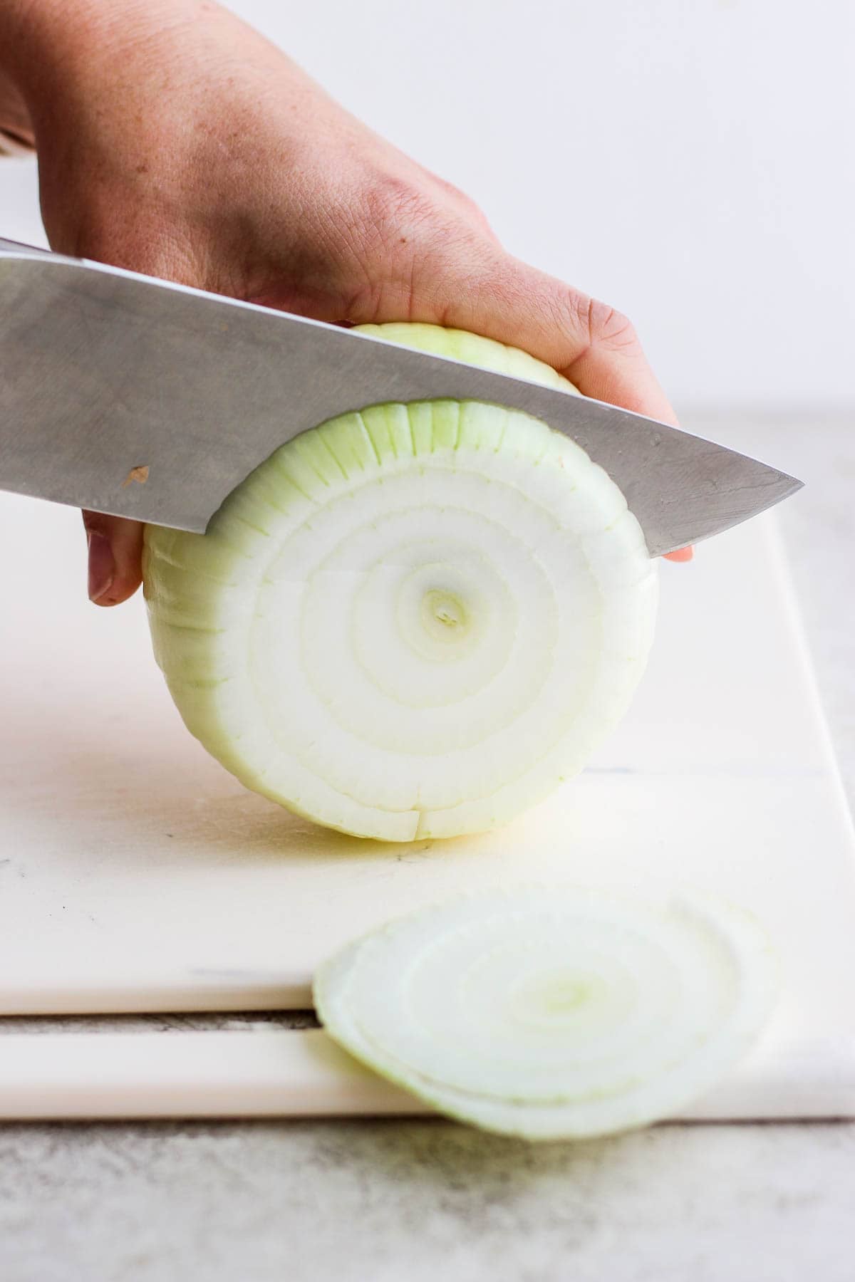 A yellow onion being cut into slices for a smoked onion dip.
