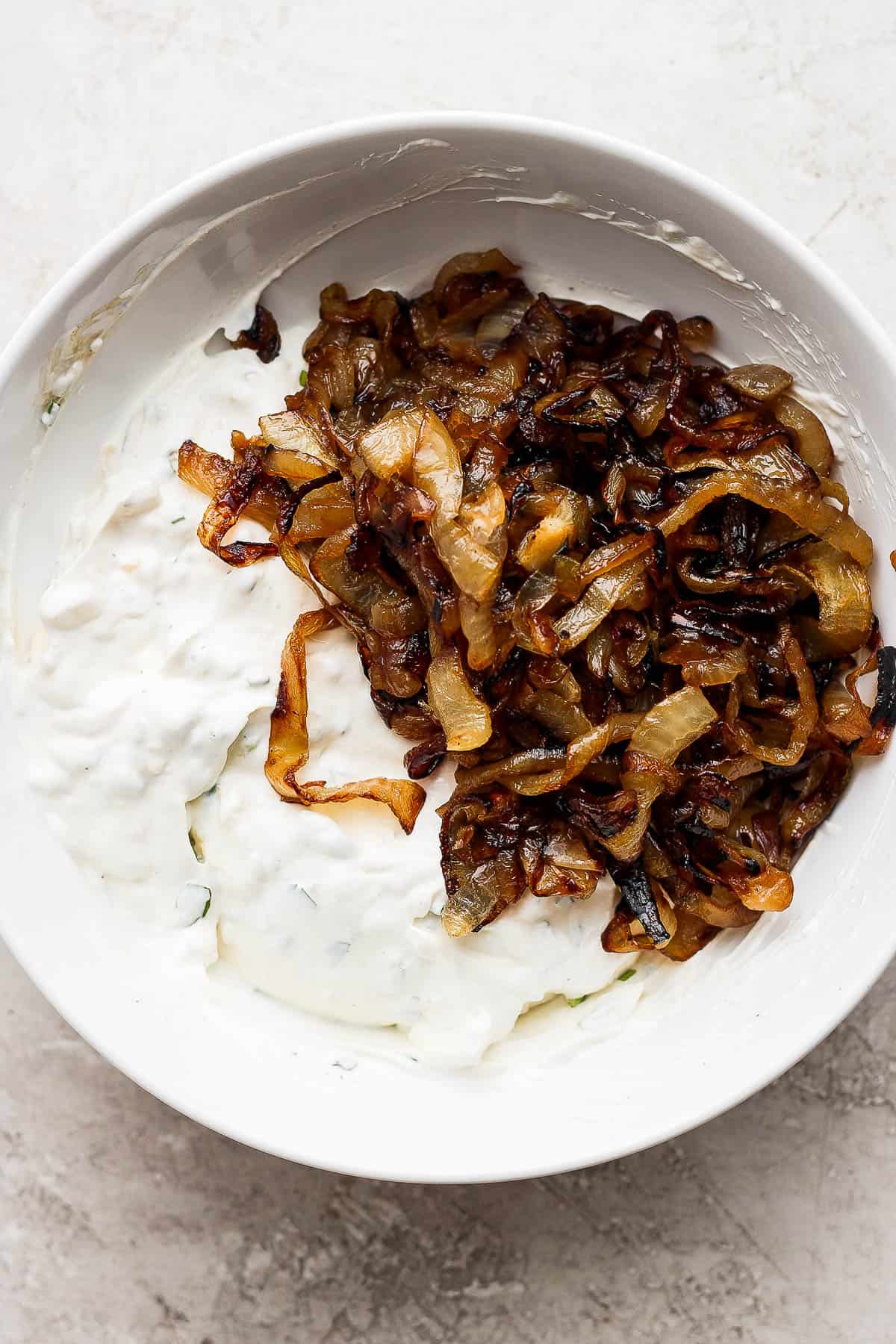 Smoked and caramelized onions added to the rest of the smoked onion dip ingredients in a white bowl.
