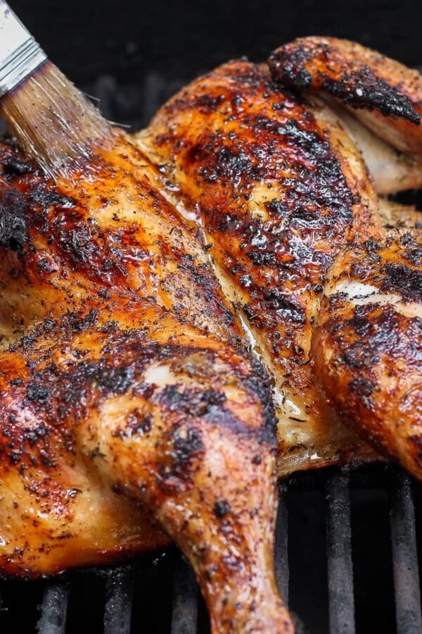 A grilled spatchcock chicken being basted on the grill.