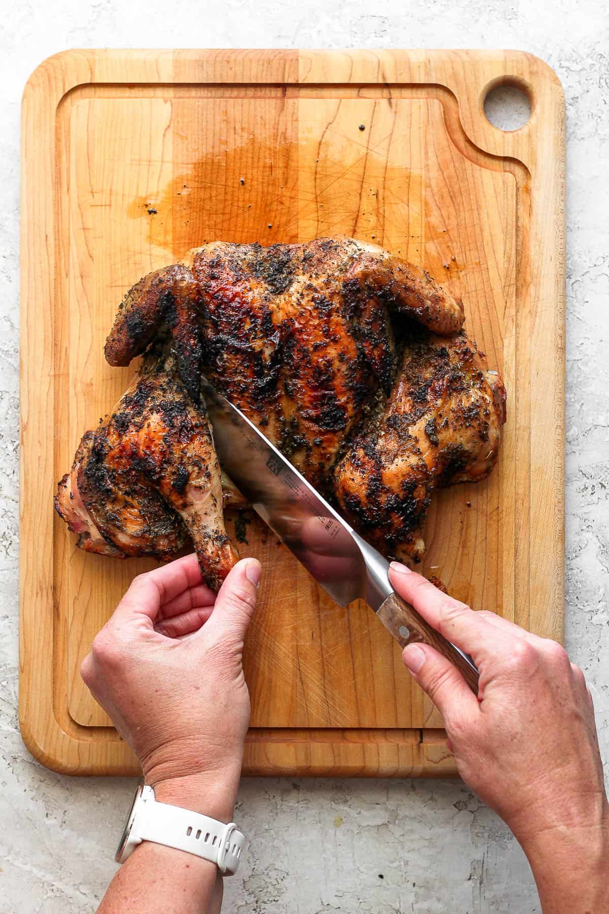 The leg quarters of a grilled spatchcock chicken being cut away from the rest of the chicken.