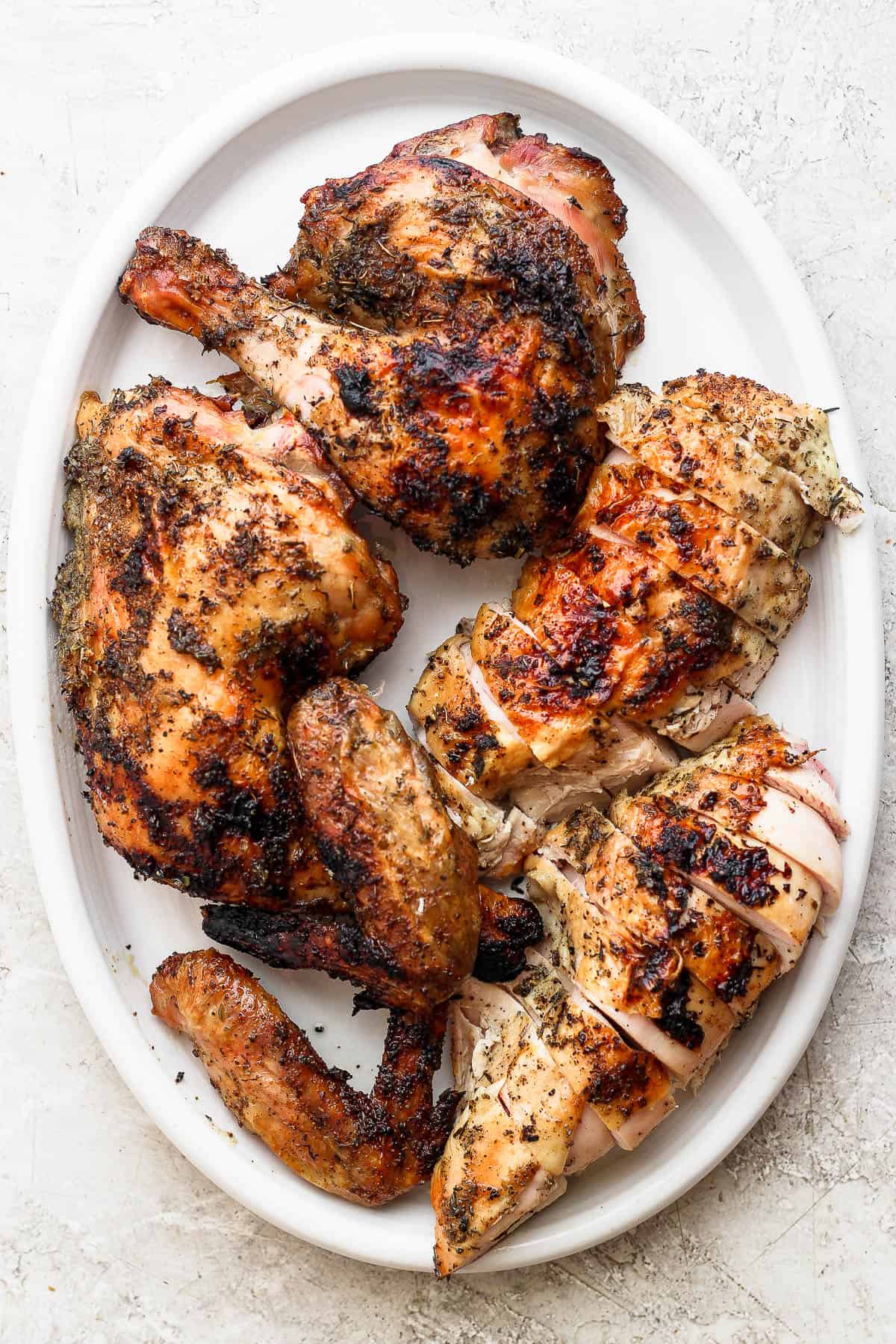 A grilled spatchcock chicken carved into sections and placed on a platter.