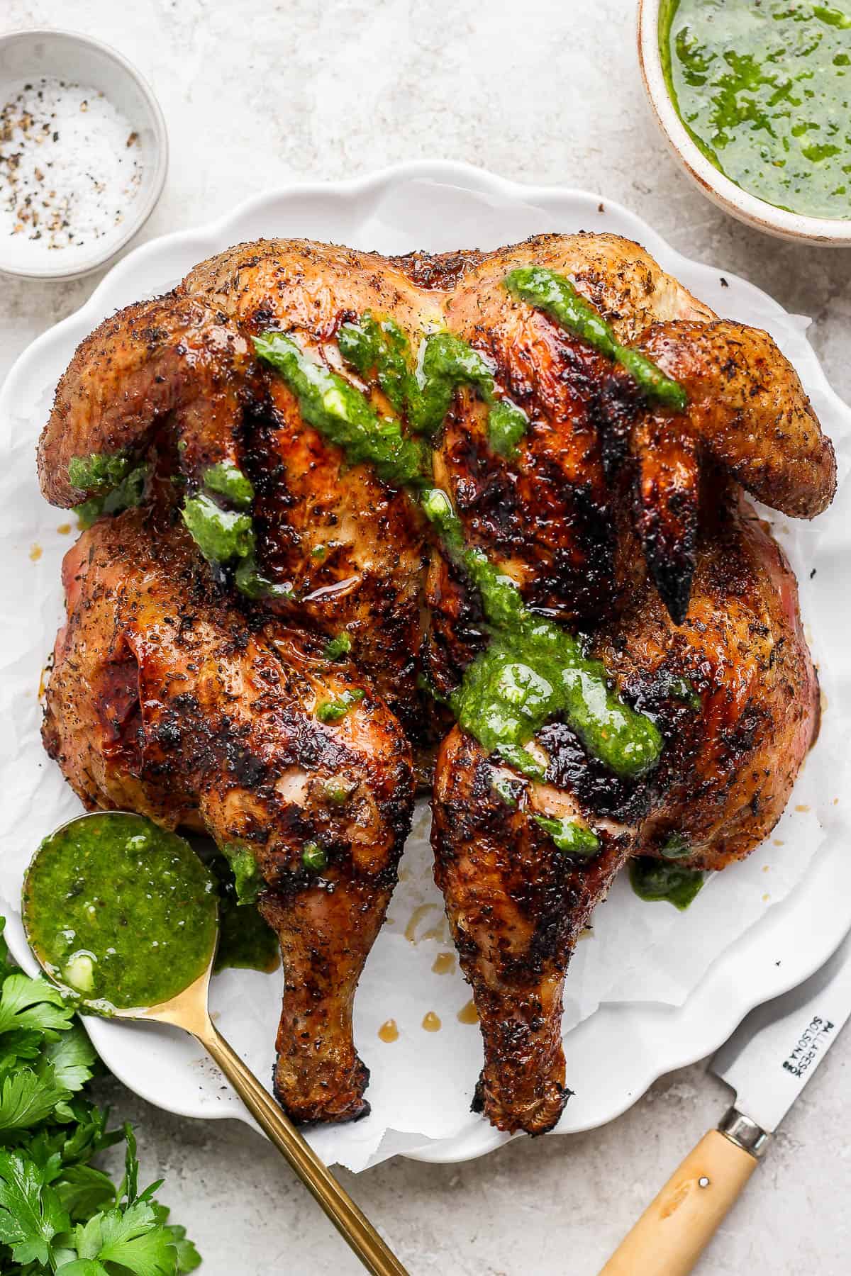 A grilled spatchcock chicken with chimichurri sauce drizzled on top.