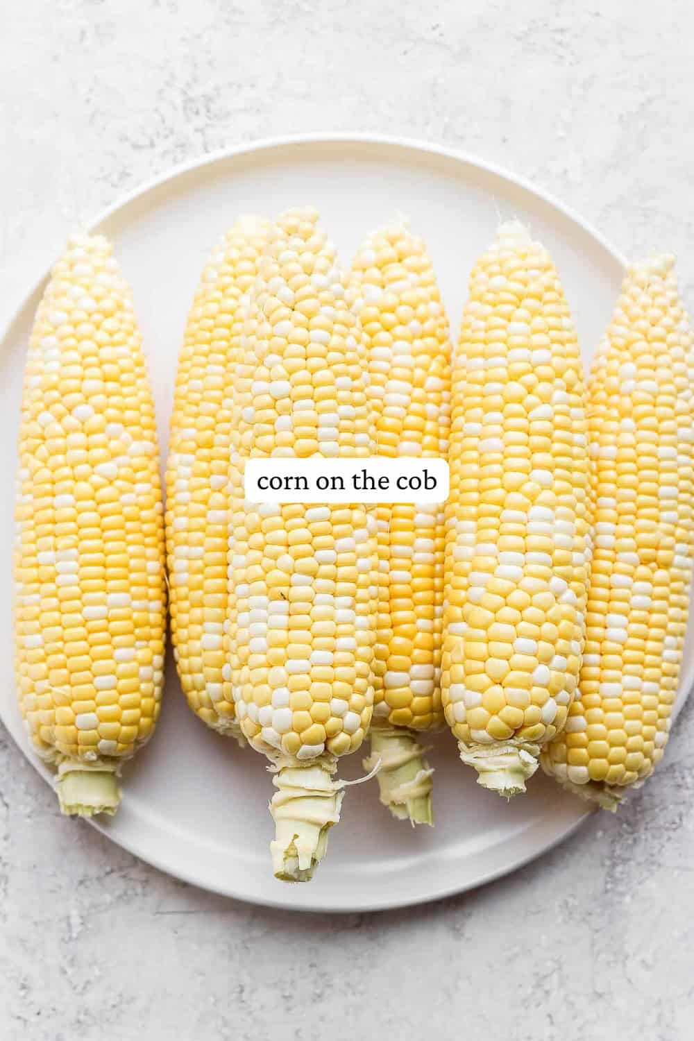 Clean ears of sweet corn on a white plate with a label.