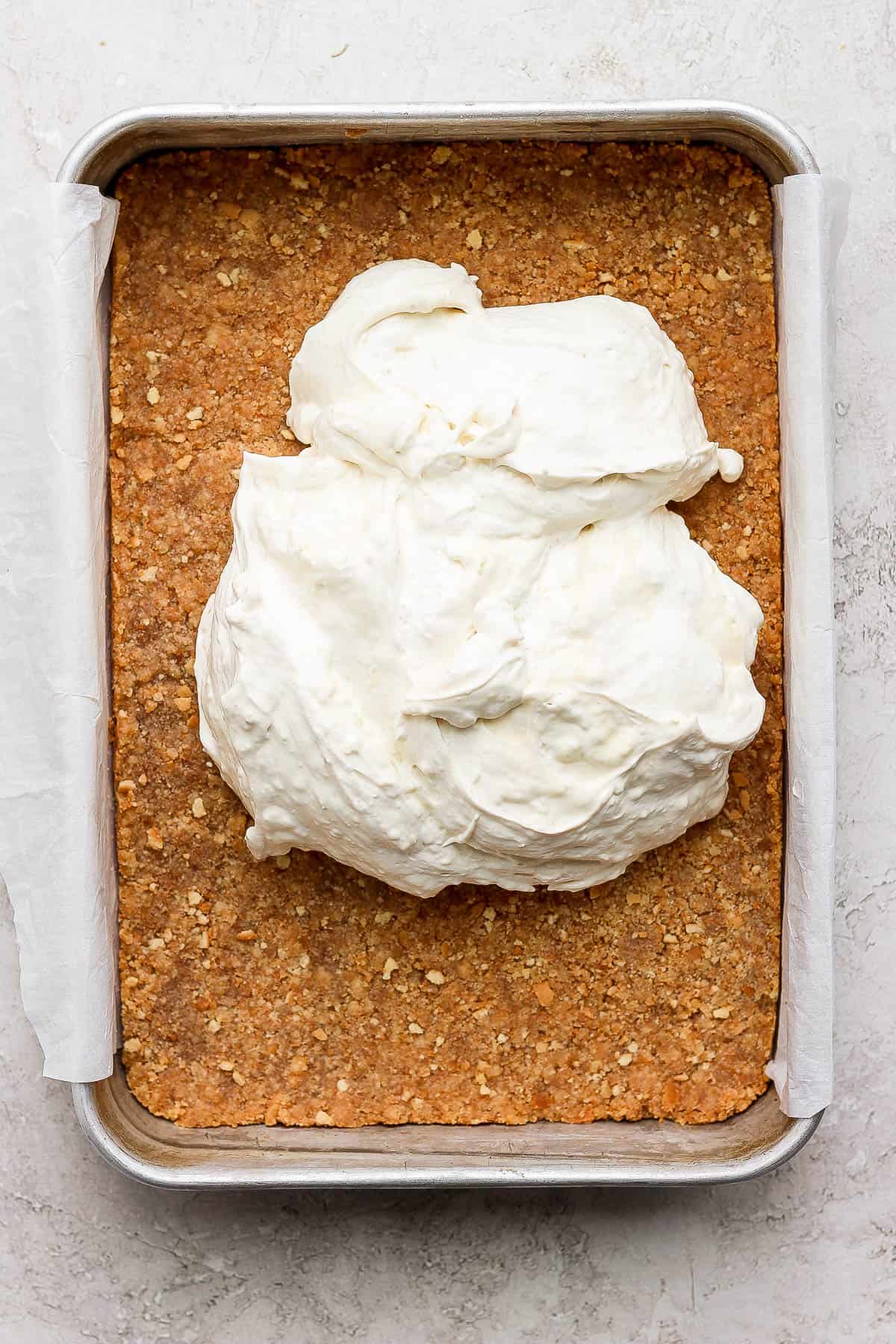 Key lime cheesecake bars filling plopped on top of the crust in a baking pan.