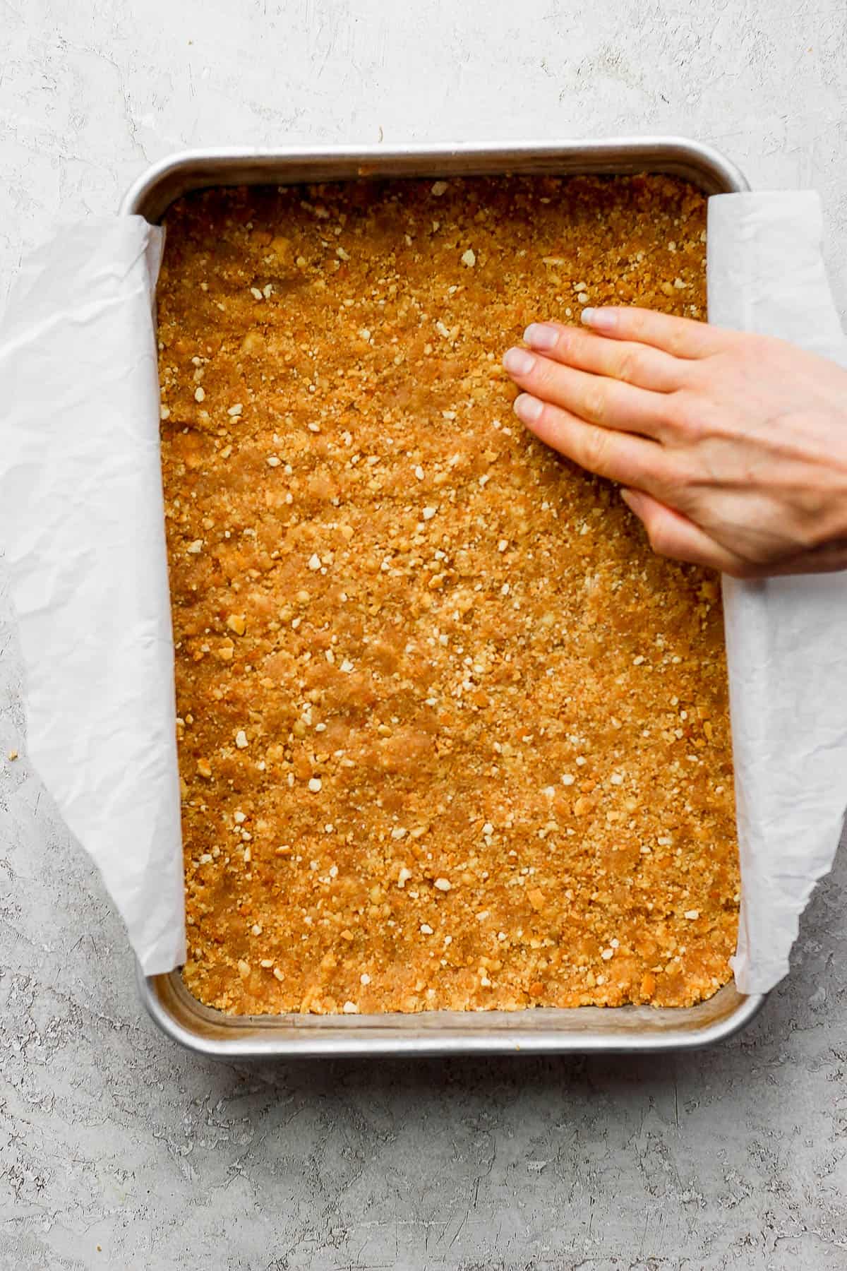The crust for key lime cheesecake bars pressed into a parchment-lined baking pan.