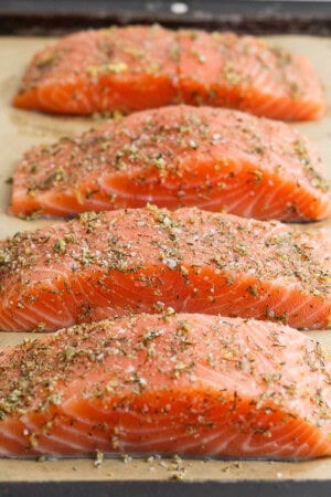Salmon seasoning on four salmon fillets on a parchment-lined sheet pan.