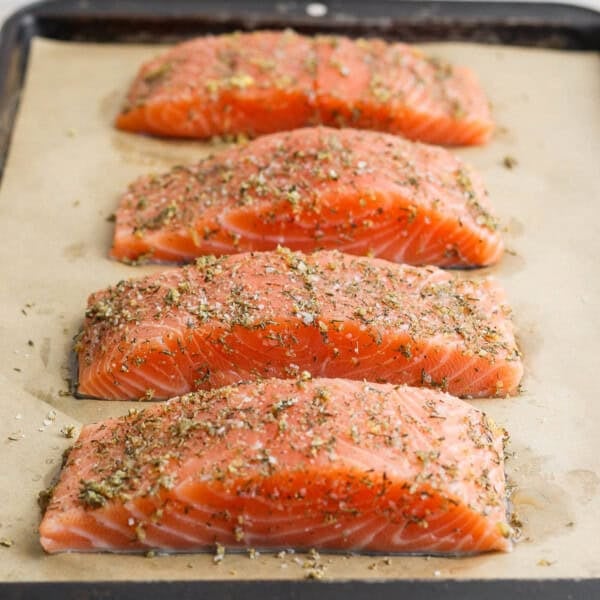 Salmon seasoning on four salmon fillets on a parchment-lined sheet pan.