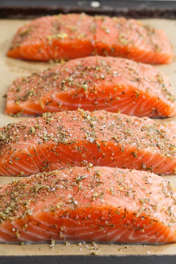 Salmon seasoning on four salmon fillets on a parchment-lined sheet pan.