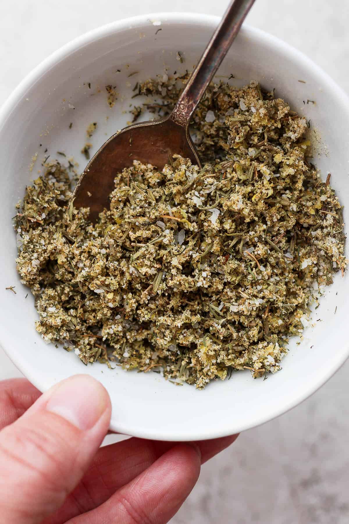A fully mixed salmon seasoning in a white bowl being held by a hand.