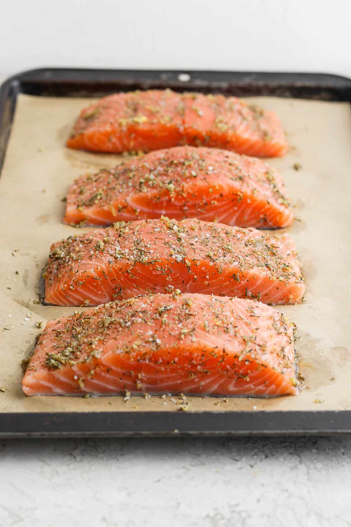 Salmon seasoning on four salmon fillets before going in the oven on a sheet pan.