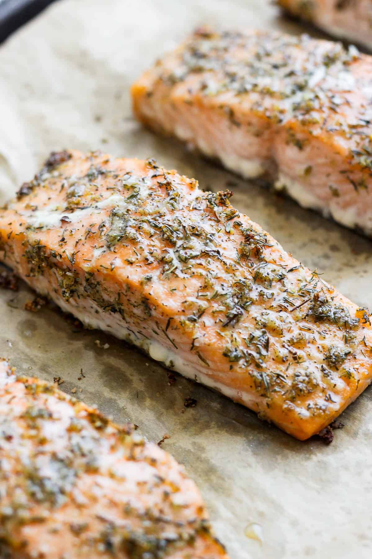 Fully baked salmon fillets on a parchment-lined sheet pan that were seasoned with salmon seasoning.