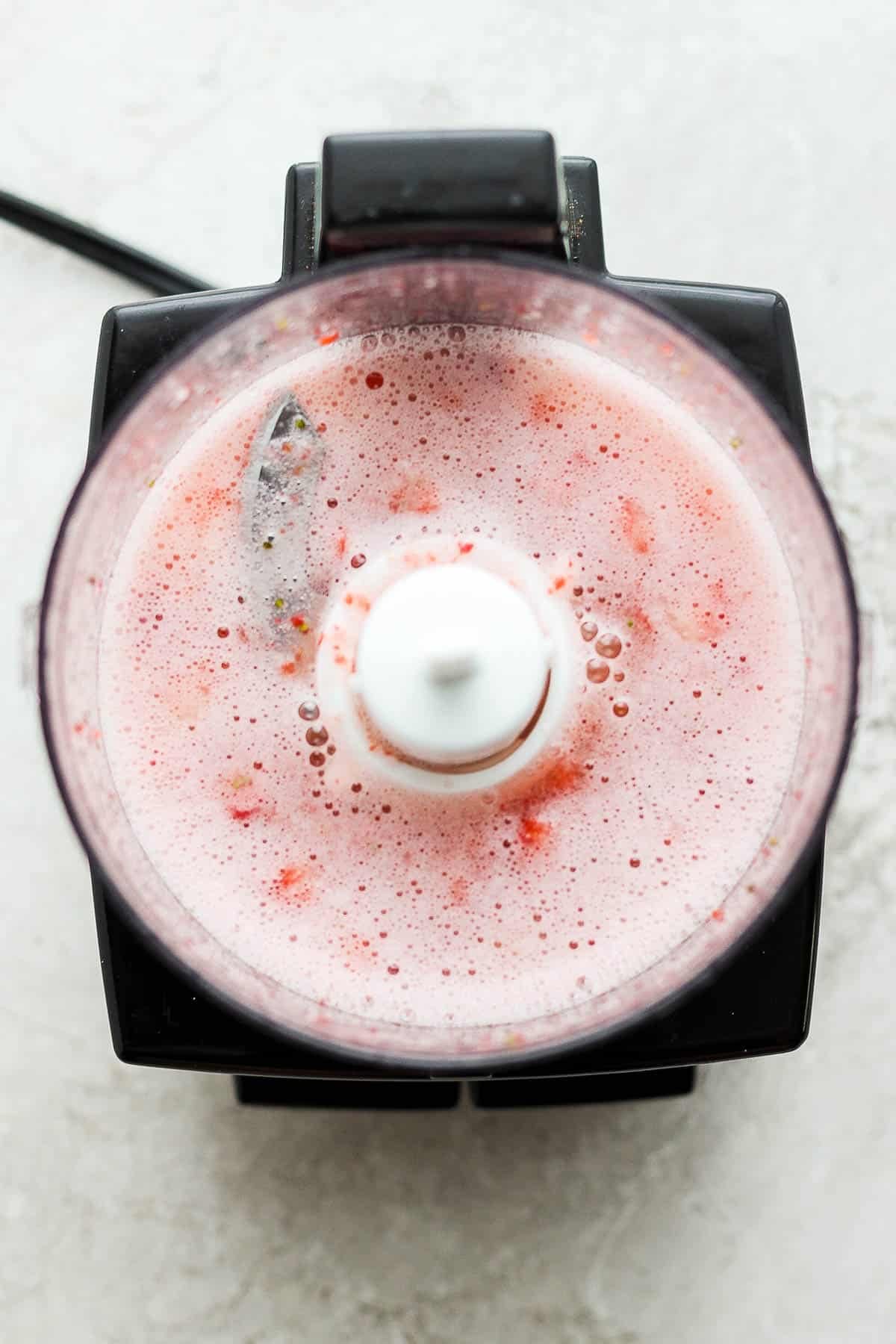 Strawberries, simple syurp, lime juice, and rum being blended in a small food processor for a strawberry mojito.
