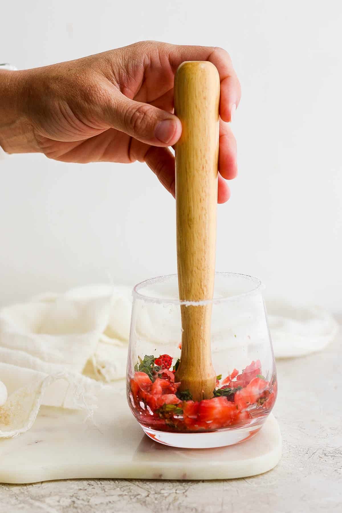 Fresh strawberries and mint being muddled in a cocktail glass for a strawberry mojito.