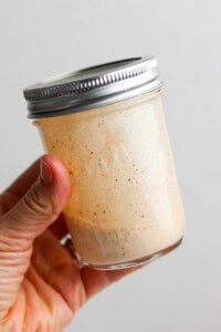 Someone holding a mason jar filled with a creamy sauce.