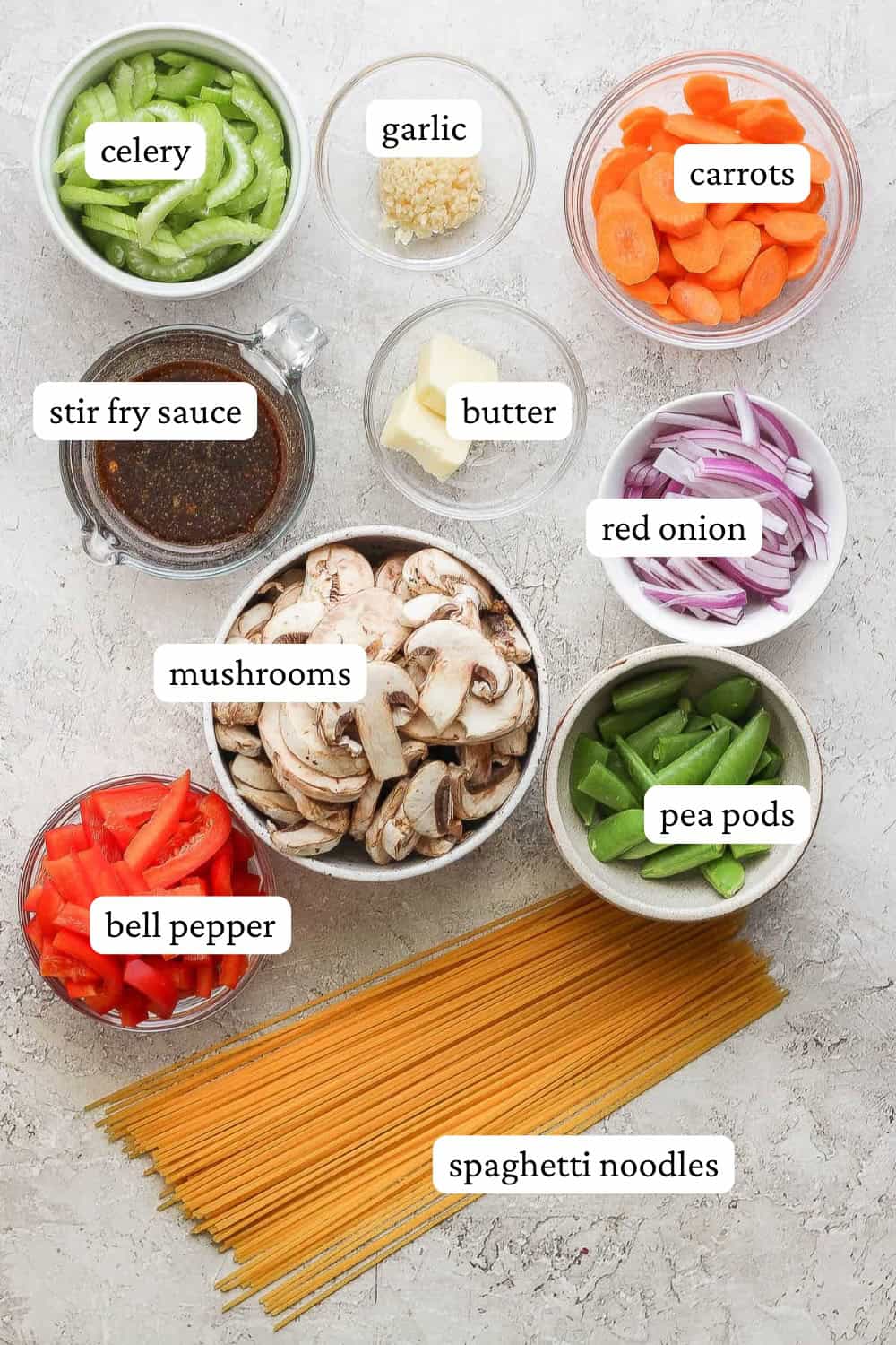 Veggie lo mein ingredients in a bowls next to some spaghetti noodles with labels.