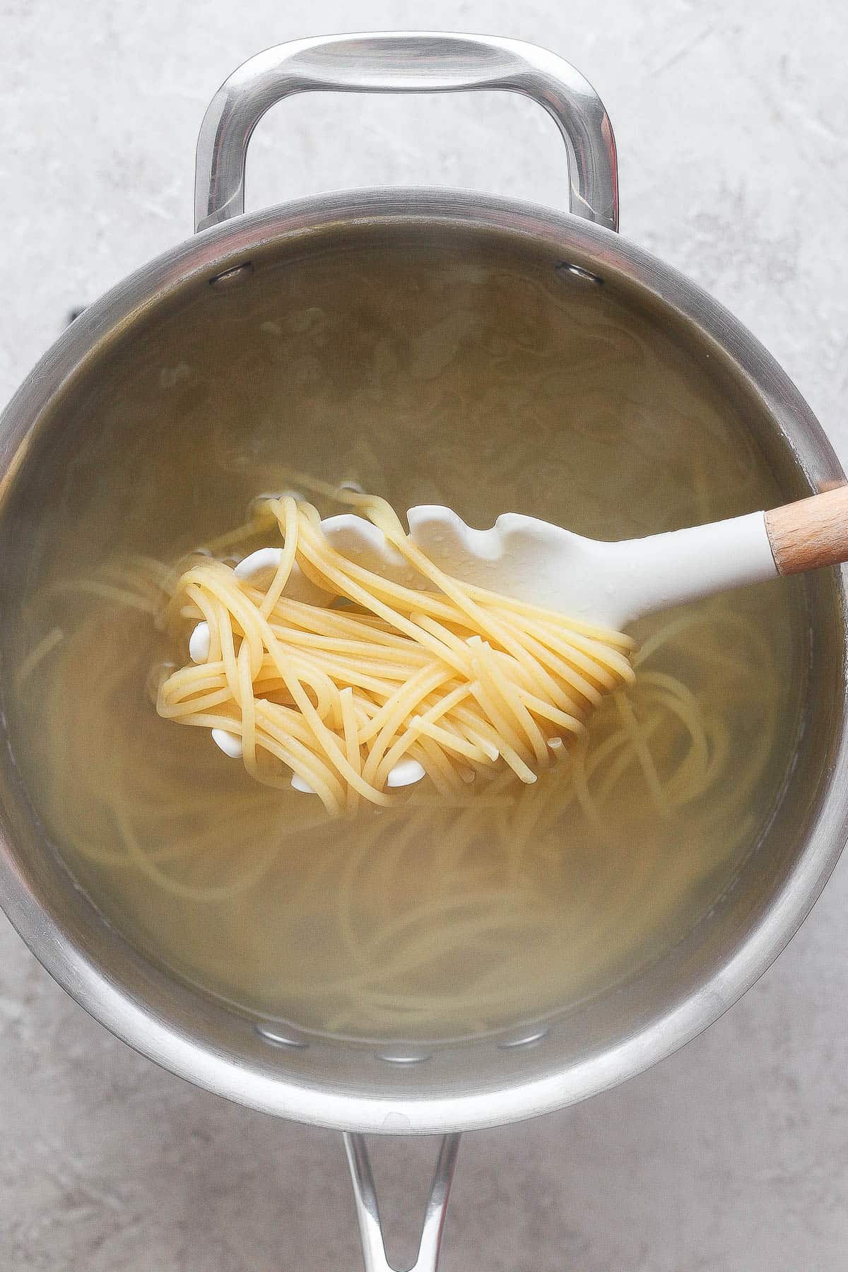 A spoon scooping up some cooked spaghetti noodles for veggie lo mein.