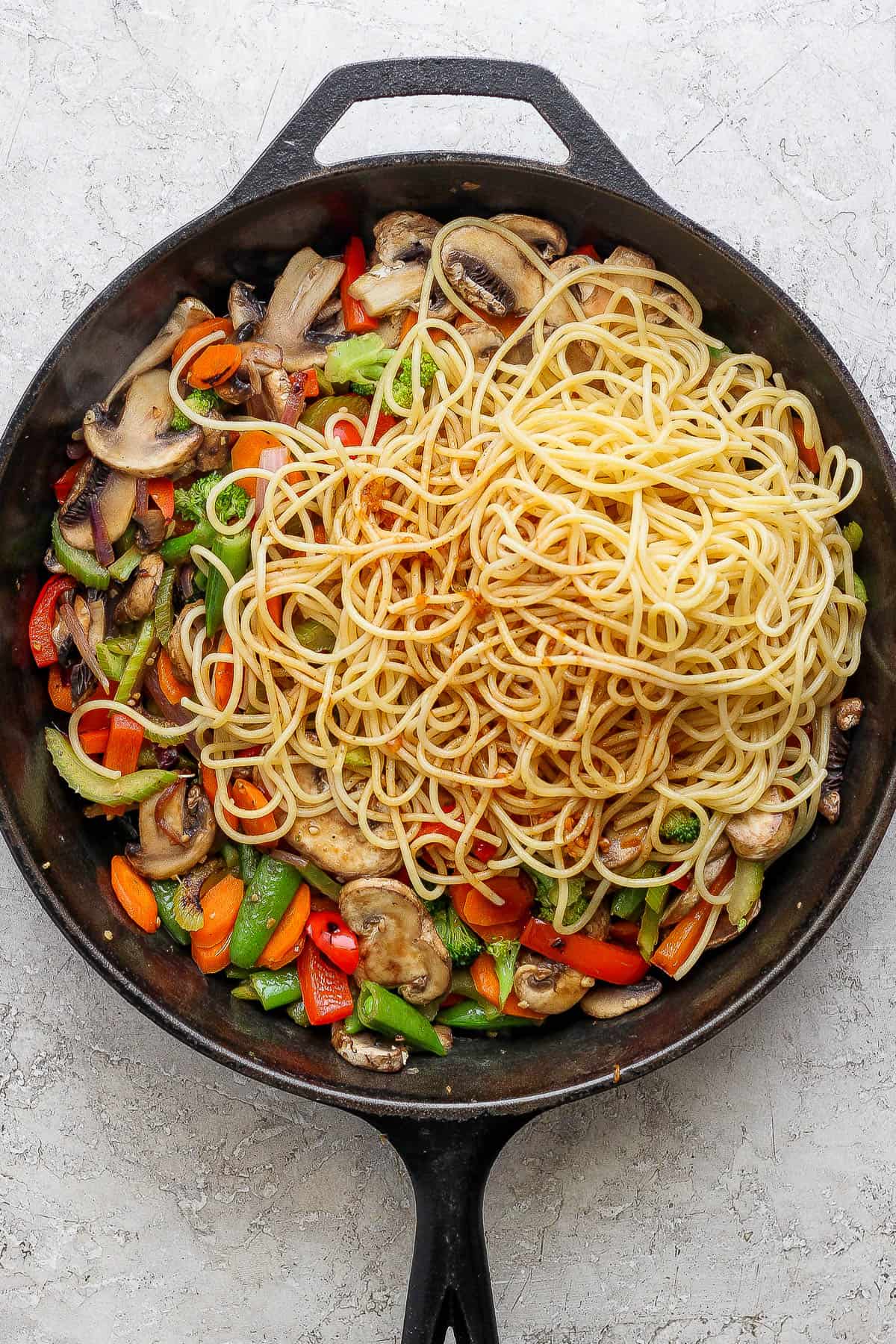 Noodles and sauce added to the veggie lo mein noodles in a skillet.
