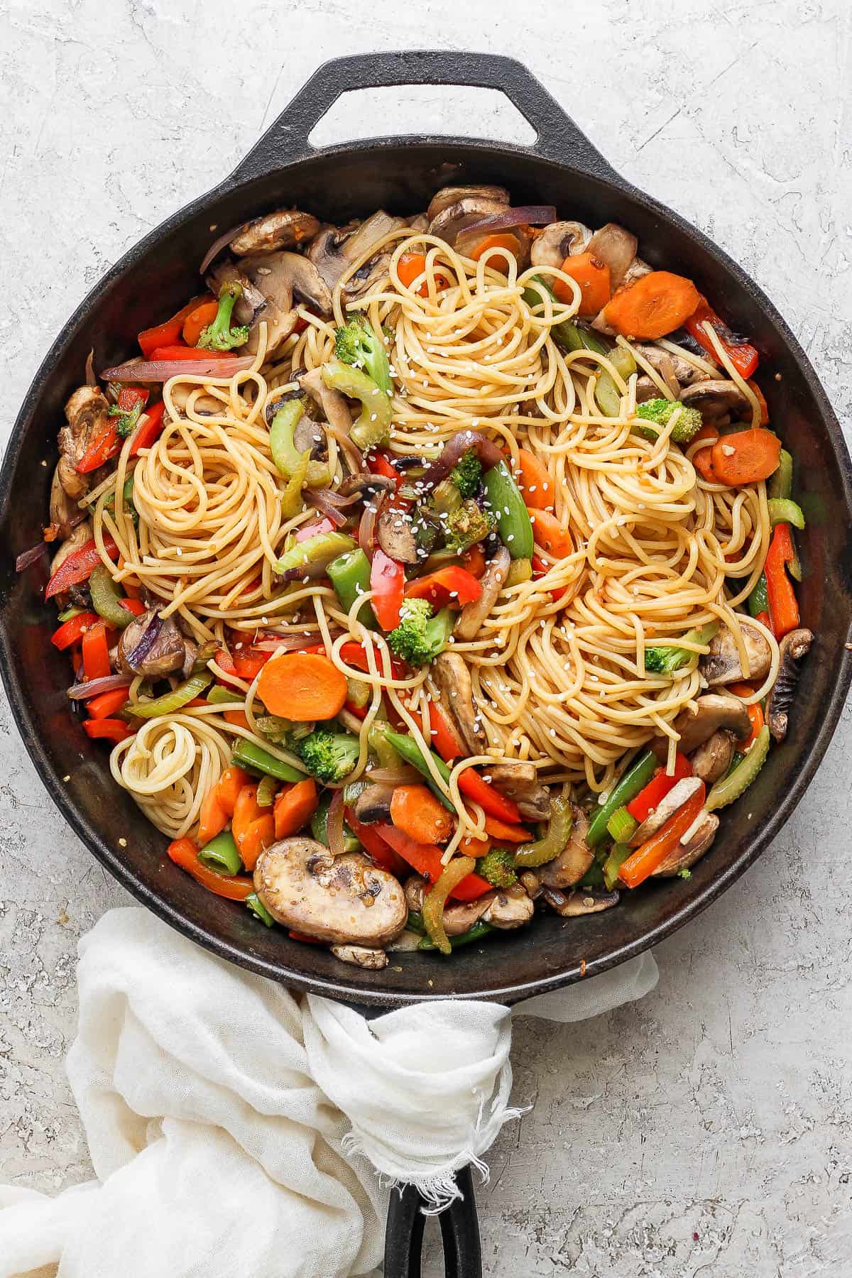 Veggie lo mein in a cast iron skillet with some sesame seeds sprinkled on top.
