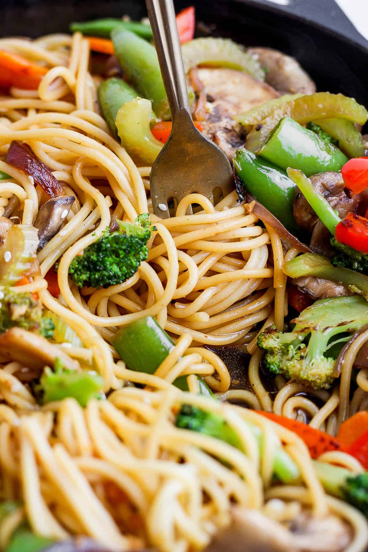 A fork twirling the noodles of veggie lo mein in a skillet.