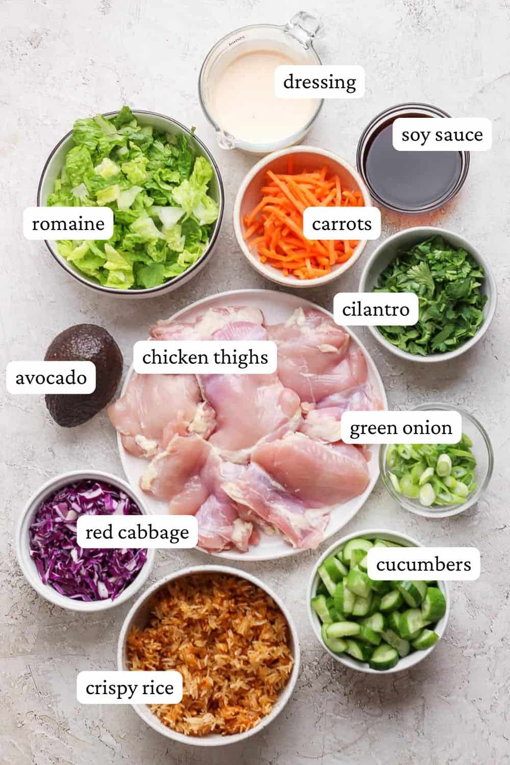 Ingredients for Bang Bang chicken salad with crispy rice in individual bowls; dressing, romaine, carrots, soy sauce, cilantro, chicken thighs, avocado, red cabbage, crispy rice, cucumbers, and green onion.