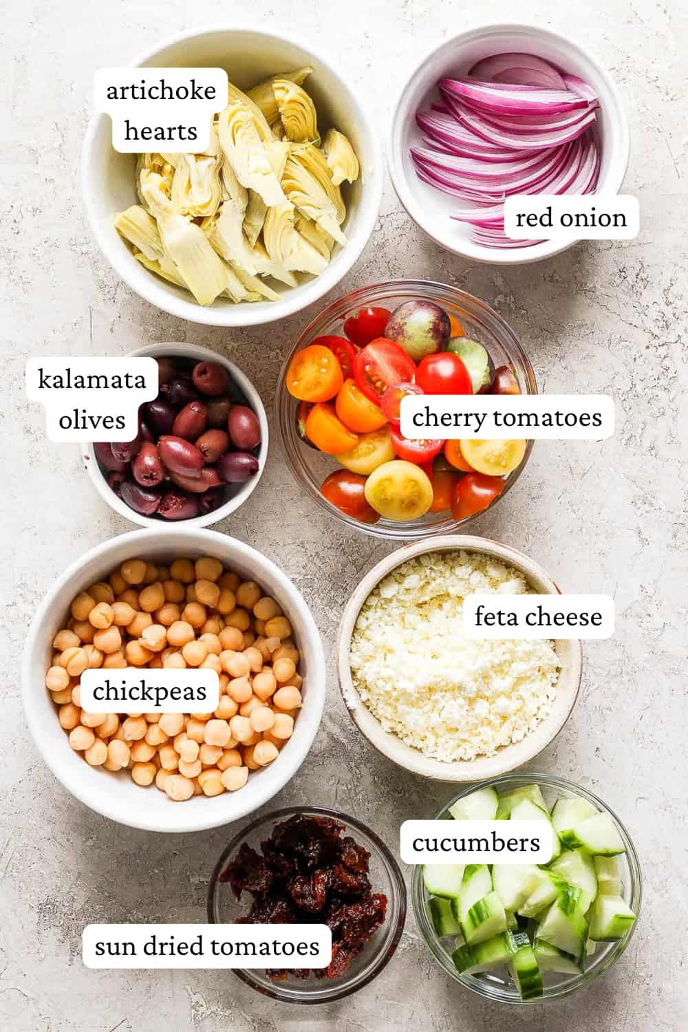 Ingredients for Greek couscous salad in separate bowls with labels.